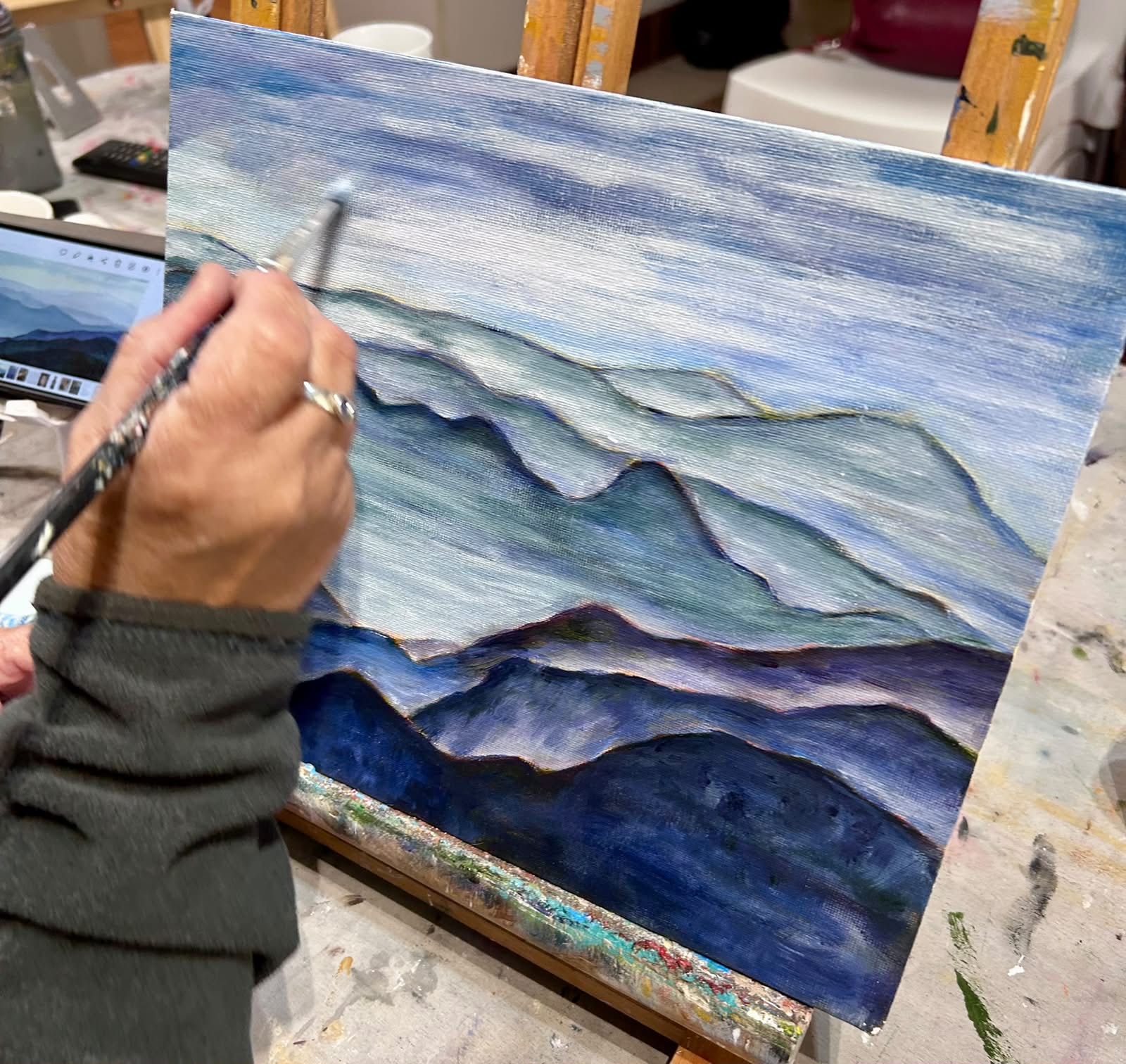 Artist painting layered blue mountain landscape