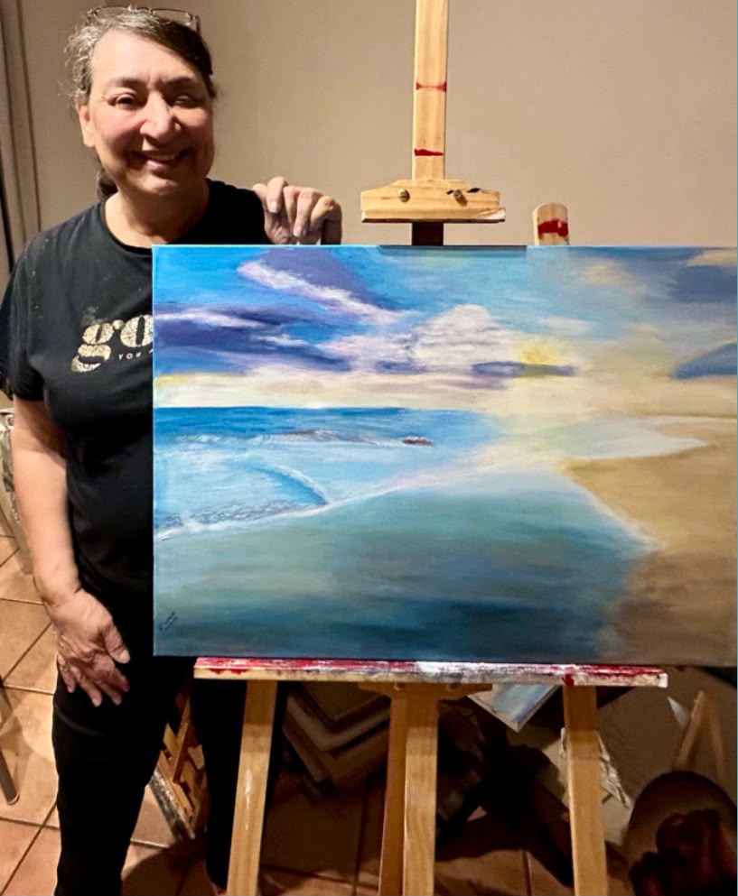Artist beaming next to her serene blue beach landscape painting